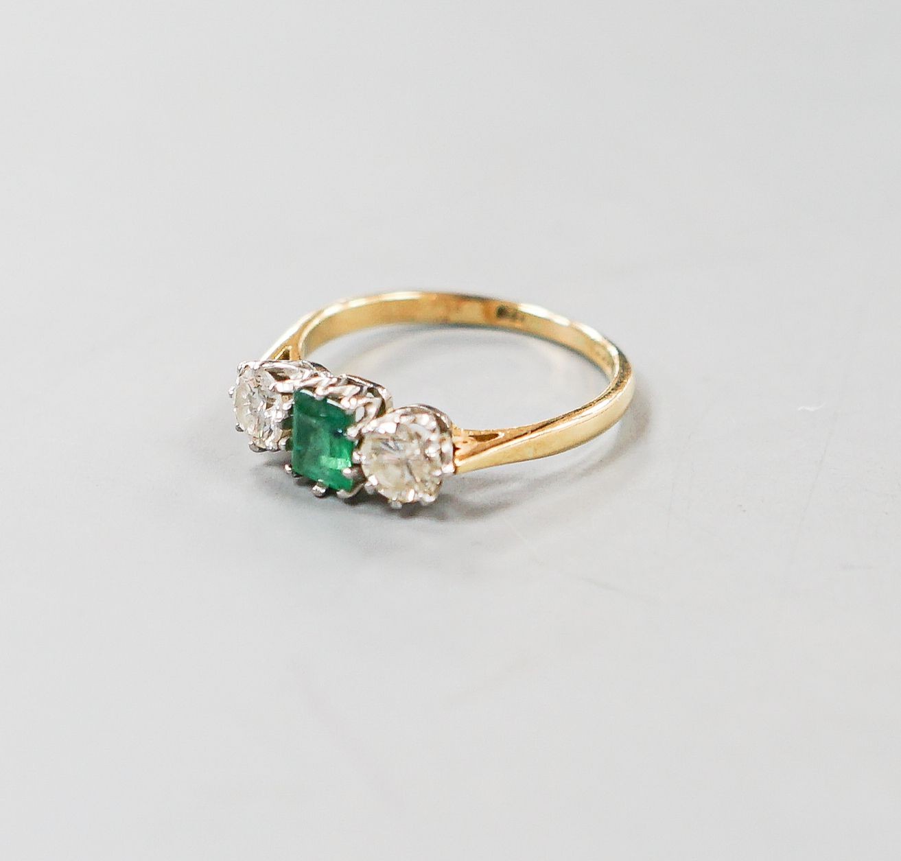 A modern 18ct gold, emerald and diamond set three stone ring, size O, gross weight 3.1 grams.